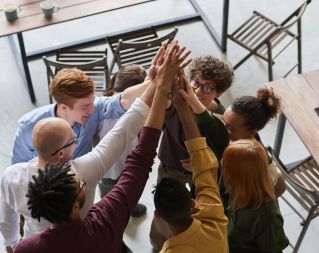 A diverse group of professionals high-fiving in a modern office, showcasing teamwork and collaboration.